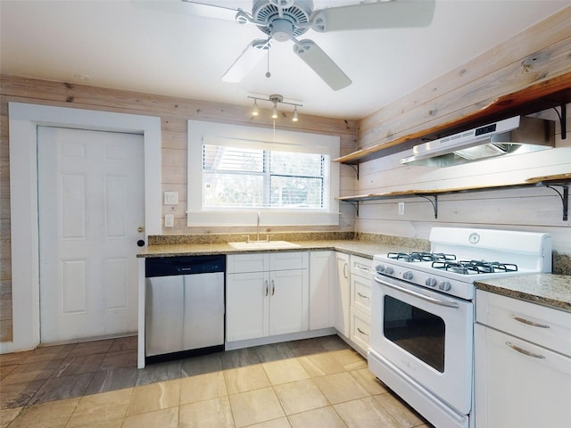 kitchen with stainless steel dishwasher, wooden walls, gas range gas stove, white cabinets, and sink