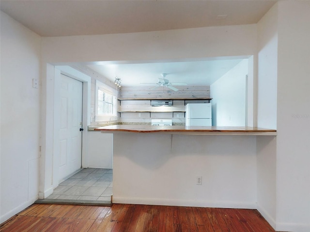 kitchen featuring white refrigerator, ceiling fan, light wood-type flooring, kitchen peninsula, and a breakfast bar area