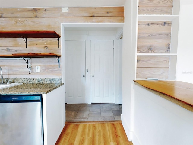 kitchen featuring stone counters, stainless steel dishwasher, light wood-type flooring, and wooden walls