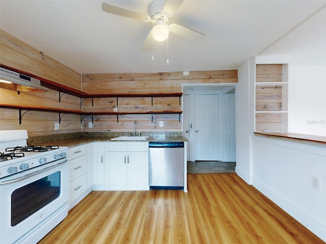 kitchen featuring dishwasher, white range with gas cooktop, wooden walls, white cabinets, and sink