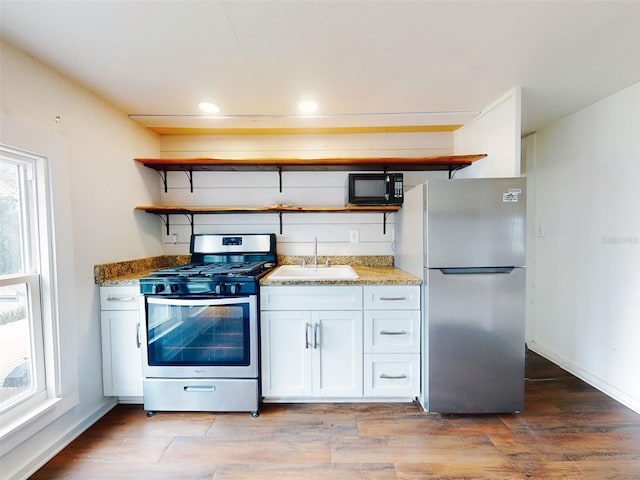 kitchen featuring a wealth of natural light, stainless steel appliances, stone countertops, white cabinetry, and sink