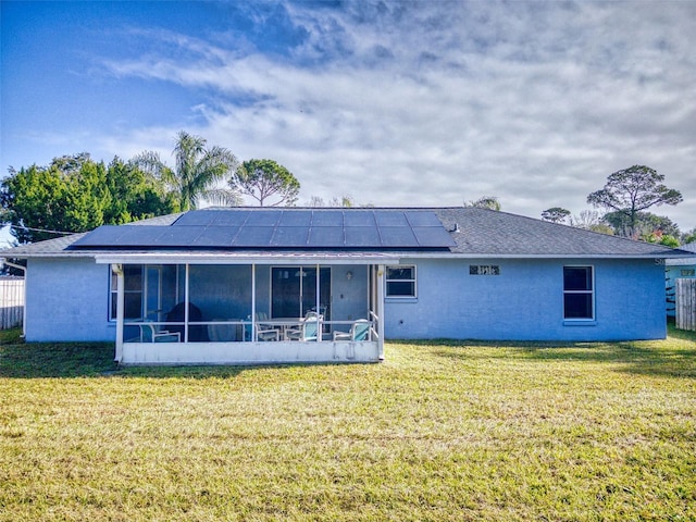 rear view of property with a yard, a sunroom, and solar panels