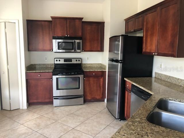 kitchen with light stone countertops, light tile patterned floors, appliances with stainless steel finishes, and sink