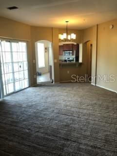 unfurnished living room with dark colored carpet, a wealth of natural light, and a chandelier