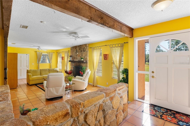 entrance foyer with a textured ceiling, a stone fireplace, light tile patterned flooring, ceiling fan, and beam ceiling