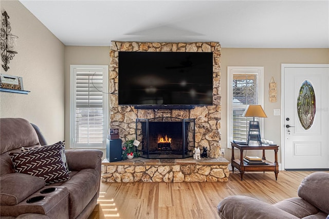 living room with a wealth of natural light, wood-type flooring, and a stone fireplace