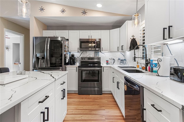 kitchen with vaulted ceiling, pendant lighting, sink, white cabinetry, and stainless steel appliances