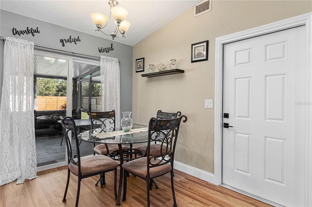 dining space featuring lofted ceiling, a notable chandelier, a textured ceiling, and light hardwood / wood-style floors