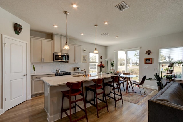 kitchen with light wood-type flooring, a breakfast bar, decorative light fixtures, a center island with sink, and black electric range