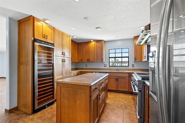 kitchen featuring wall chimney exhaust hood, a center island, stainless steel appliances, wine cooler, and sink