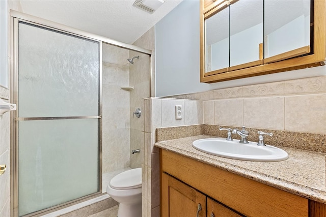 bathroom with toilet, a textured ceiling, tile walls, a shower with door, and vanity