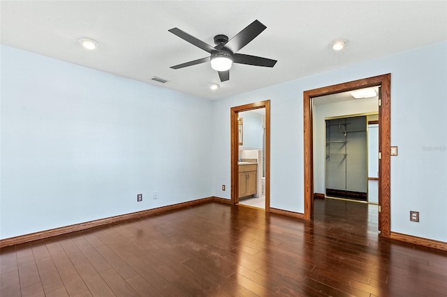 unfurnished bedroom featuring a closet, connected bathroom, dark hardwood / wood-style flooring, a walk in closet, and ceiling fan