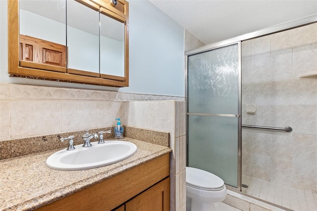 bathroom featuring tile walls, a shower with shower door, tasteful backsplash, toilet, and vanity