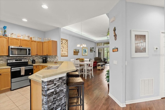 kitchen with kitchen peninsula, backsplash, stainless steel appliances, sink, and pendant lighting