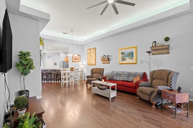 living room with a tray ceiling, wood-type flooring, and ceiling fan with notable chandelier