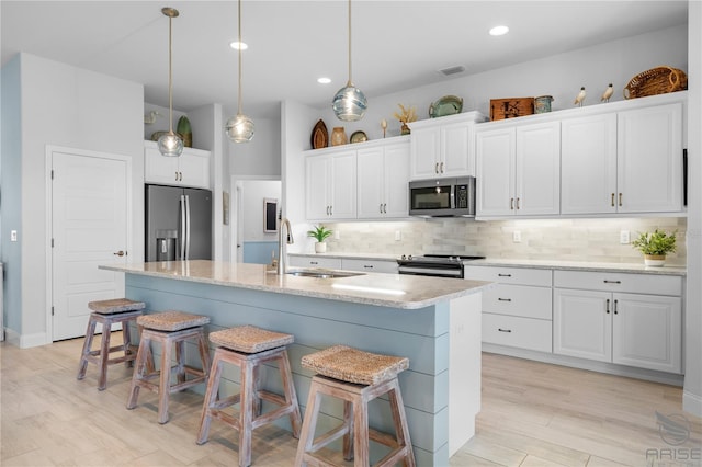 kitchen featuring sink, stainless steel appliances, white cabinetry, and an island with sink