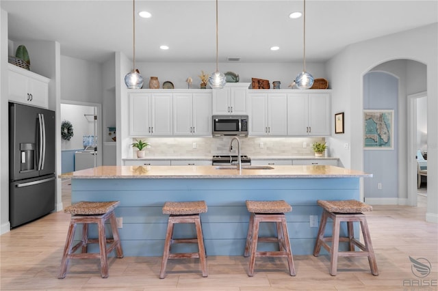 kitchen featuring black fridge, white cabinets, a kitchen island with sink, and pendant lighting