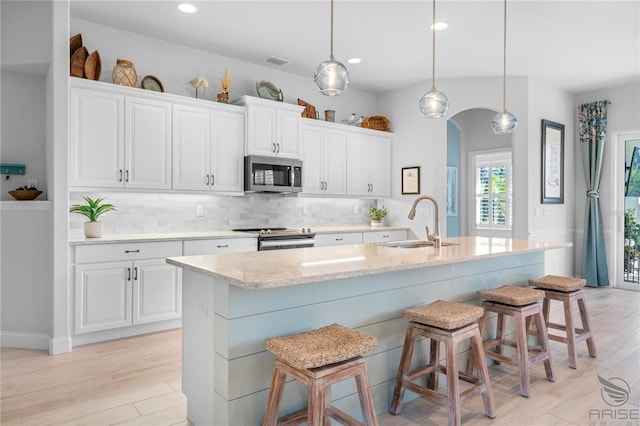 kitchen featuring white cabinets, a kitchen island with sink, stainless steel appliances, sink, and decorative light fixtures