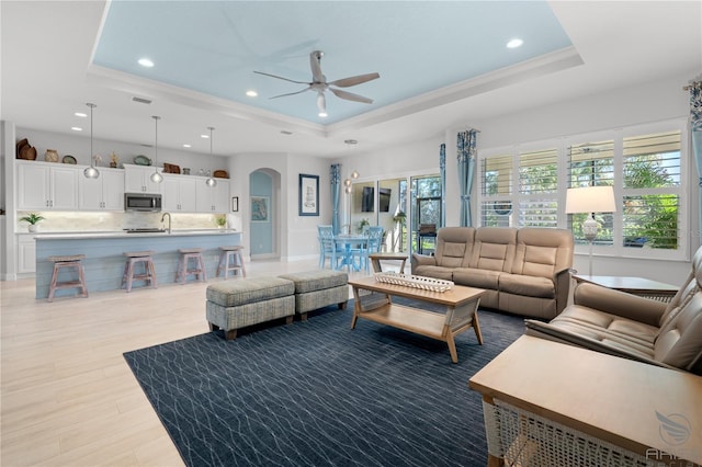 living room featuring ceiling fan, a tray ceiling, and light wood-type flooring