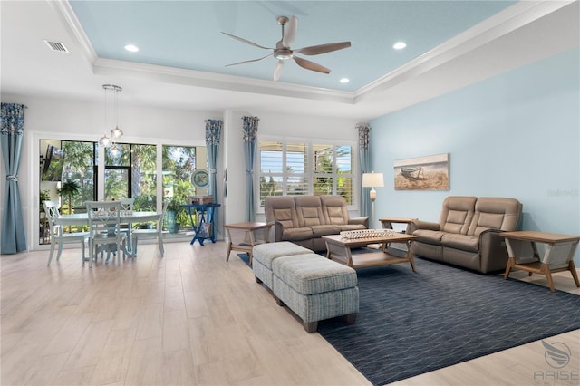 living room with ornamental molding, light wood-type flooring, and a raised ceiling