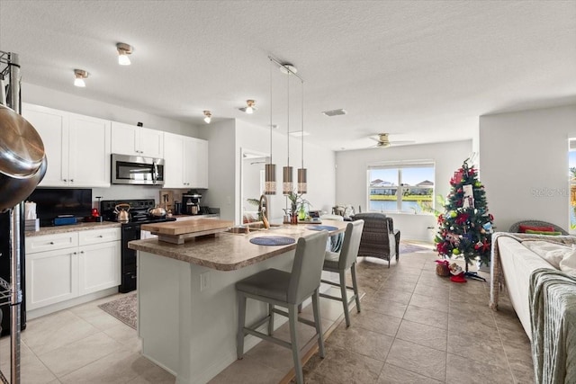 kitchen with sink, a water view, hanging light fixtures, electric range, and a kitchen island with sink