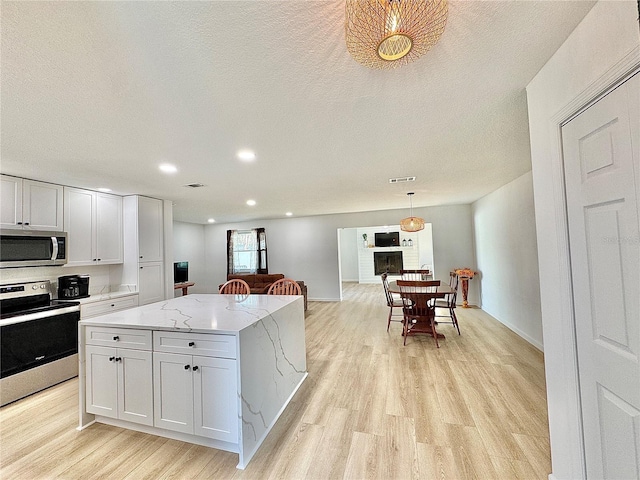 kitchen with appliances with stainless steel finishes, pendant lighting, light stone counters, light hardwood / wood-style flooring, and white cabinetry