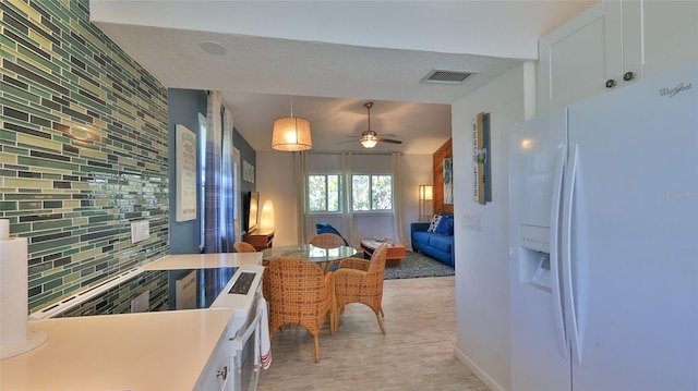 kitchen with ceiling fan, white fridge with ice dispenser, white cabinets, and decorative backsplash