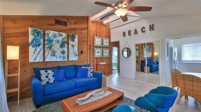 living room with vaulted ceiling, light hardwood / wood-style floors, ceiling fan, and wood walls