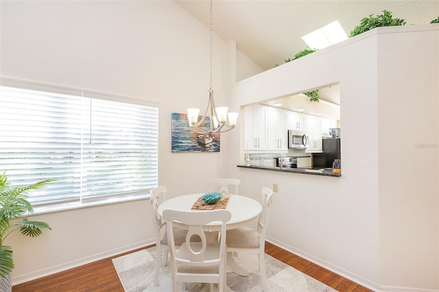 dining area with a notable chandelier, light hardwood / wood-style floors, and high vaulted ceiling