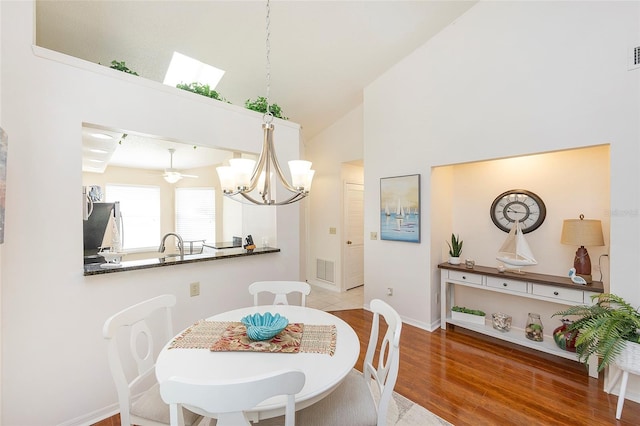 dining space with wood-type flooring, a skylight, high vaulted ceiling, sink, and ceiling fan with notable chandelier