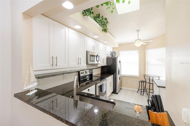 kitchen with kitchen peninsula, stainless steel appliances, white cabinetry, dark stone counters, and ceiling fan