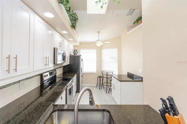 kitchen with stainless steel appliances, dark stone countertops, white cabinetry, ceiling fan, and sink