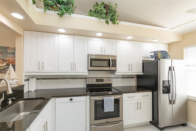 kitchen featuring sink, stainless steel appliances, dark stone countertops, and white cabinetry