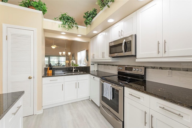 kitchen with stainless steel appliances, sink, decorative light fixtures, white cabinetry, and an inviting chandelier