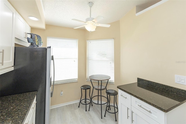 kitchen featuring white cabinets, stainless steel fridge, dark stone counters, and light hardwood / wood-style floors