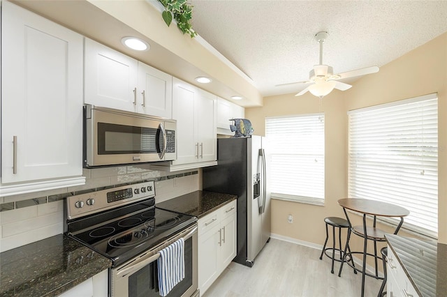 kitchen featuring stainless steel appliances, white cabinets, a textured ceiling, decorative backsplash, and dark stone counters