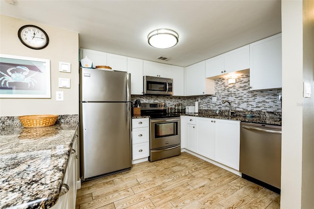 kitchen with light wood-type flooring, appliances with stainless steel finishes, dark stone countertops, and white cabinetry