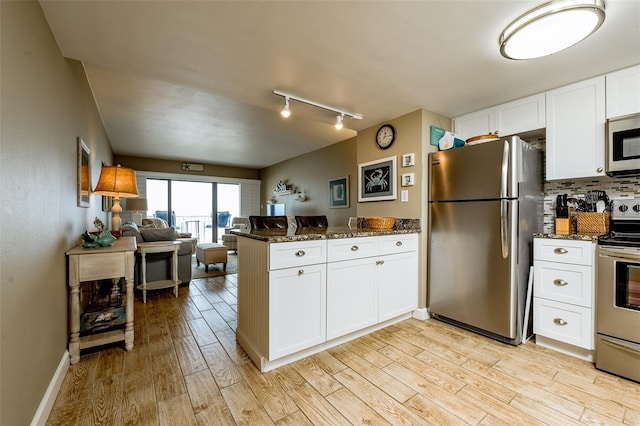 kitchen with stainless steel appliances, dark stone counters, rail lighting, and white cabinets