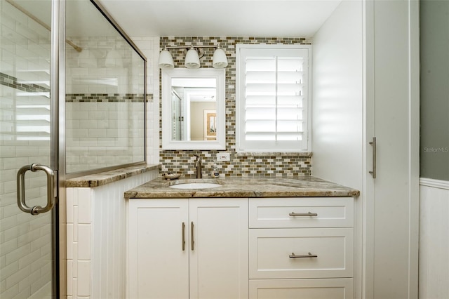 bathroom featuring vanity, a shower with shower door, and tasteful backsplash