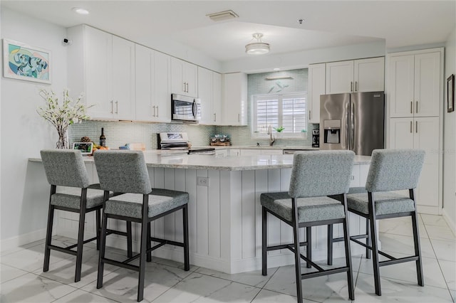 kitchen featuring white cabinetry, sink, a breakfast bar area, backsplash, and stainless steel appliances