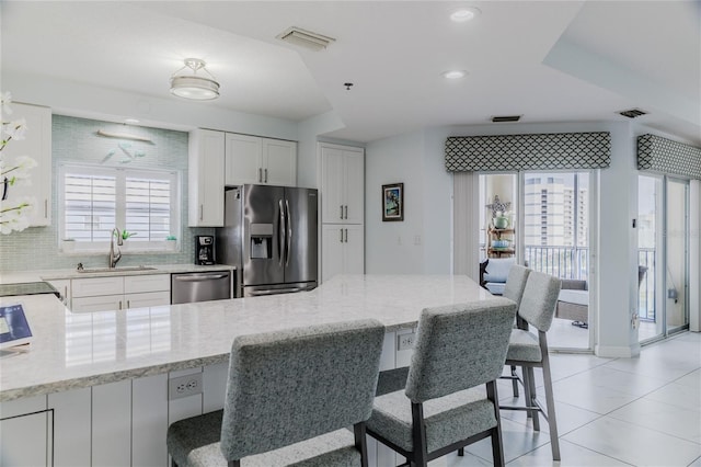 kitchen with sink, stainless steel appliances, light stone counters, a kitchen bar, and decorative backsplash