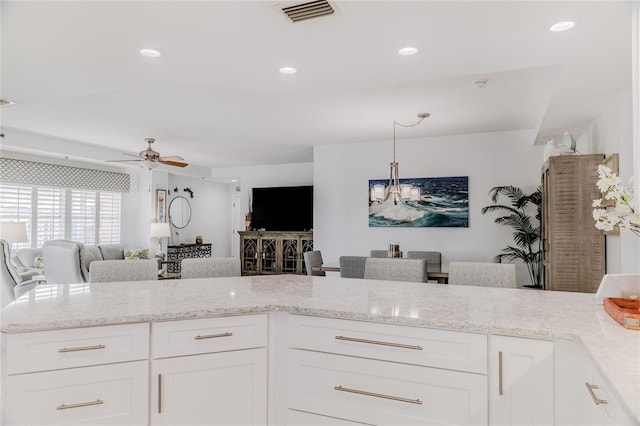 kitchen featuring pendant lighting, ceiling fan with notable chandelier, white cabinets, and light stone counters