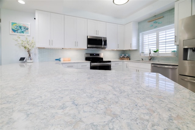 kitchen featuring white cabinetry, sink, light stone counters, and appliances with stainless steel finishes