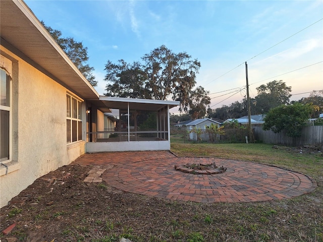 yard at dusk featuring a sunroom, a patio area, and an outdoor fire pit