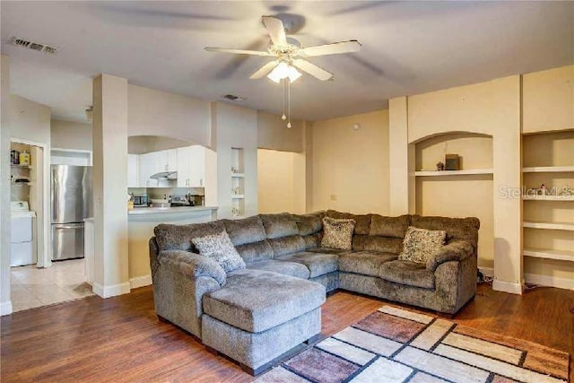 living room featuring ceiling fan, built in shelves, hardwood / wood-style flooring, and washer / clothes dryer