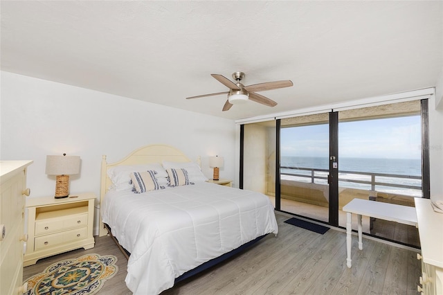 bedroom with access to outside, hardwood / wood-style flooring, ceiling fan, and a water view