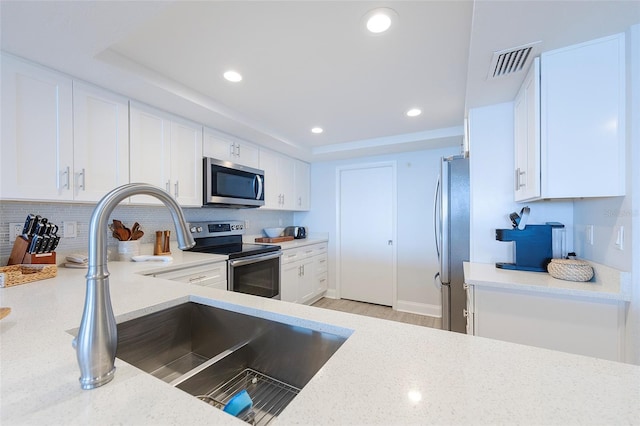 kitchen with stainless steel appliances, white cabinets, decorative backsplash, and light stone countertops