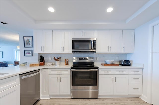 kitchen with stainless steel appliances, white cabinets, light wood-type flooring, and tasteful backsplash