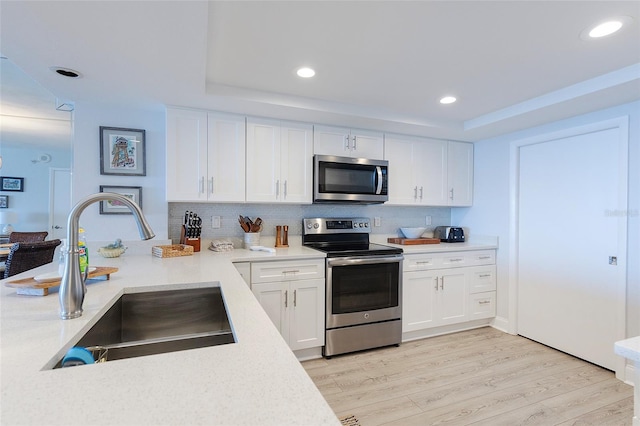 kitchen featuring sink, white cabinets, light hardwood / wood-style flooring, a tray ceiling, and appliances with stainless steel finishes