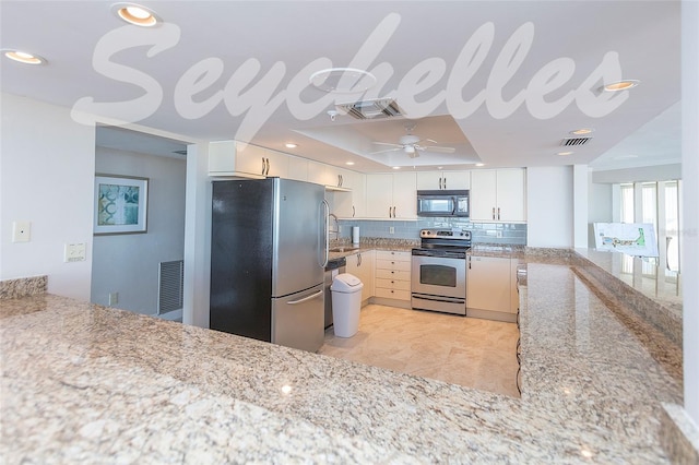 kitchen with light stone counters, decorative backsplash, white cabinets, appliances with stainless steel finishes, and ceiling fan